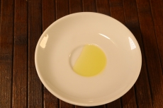 Olio di jojoba in un piattino. Se ne evidenzia il colore giallo paglierino e la viscosità media.
